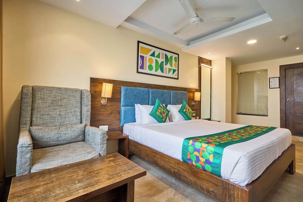 Hotelkamer met een bed, een stoel, een tafel, een plafondventilator en een kunstwerk aan de muur.
