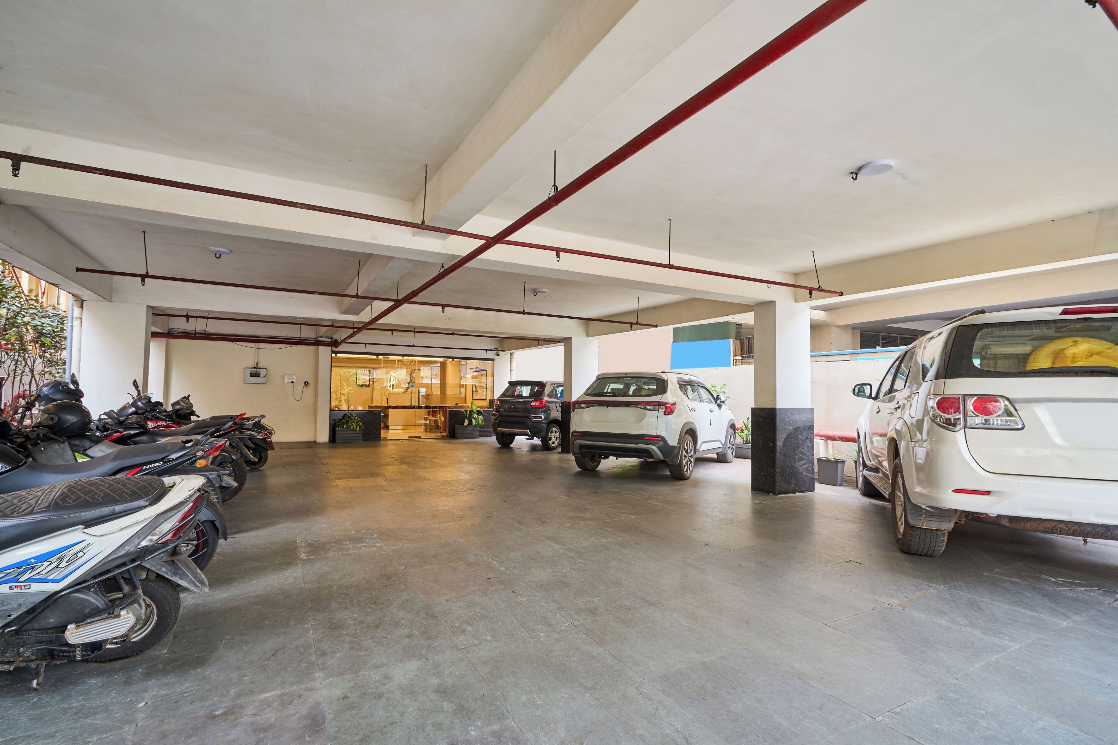 A parking garage with multiple vehicles, including motorcycles and cars, and a visible entrance to another area.