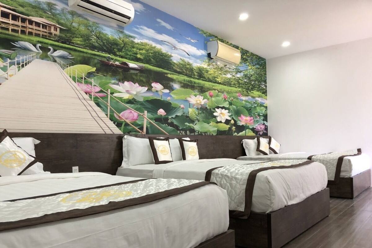 Habitación de hotel con tres camas, un mural de un estanque con cisnes y una escalera que conduce a un balcón.