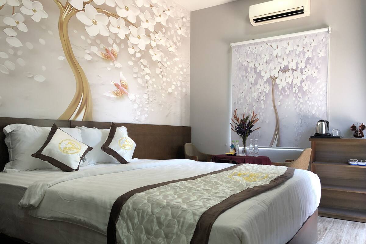 Habitación de hotel con una cama grande, una mesita de noche, un aparador de madera y una pared con diseño floral.