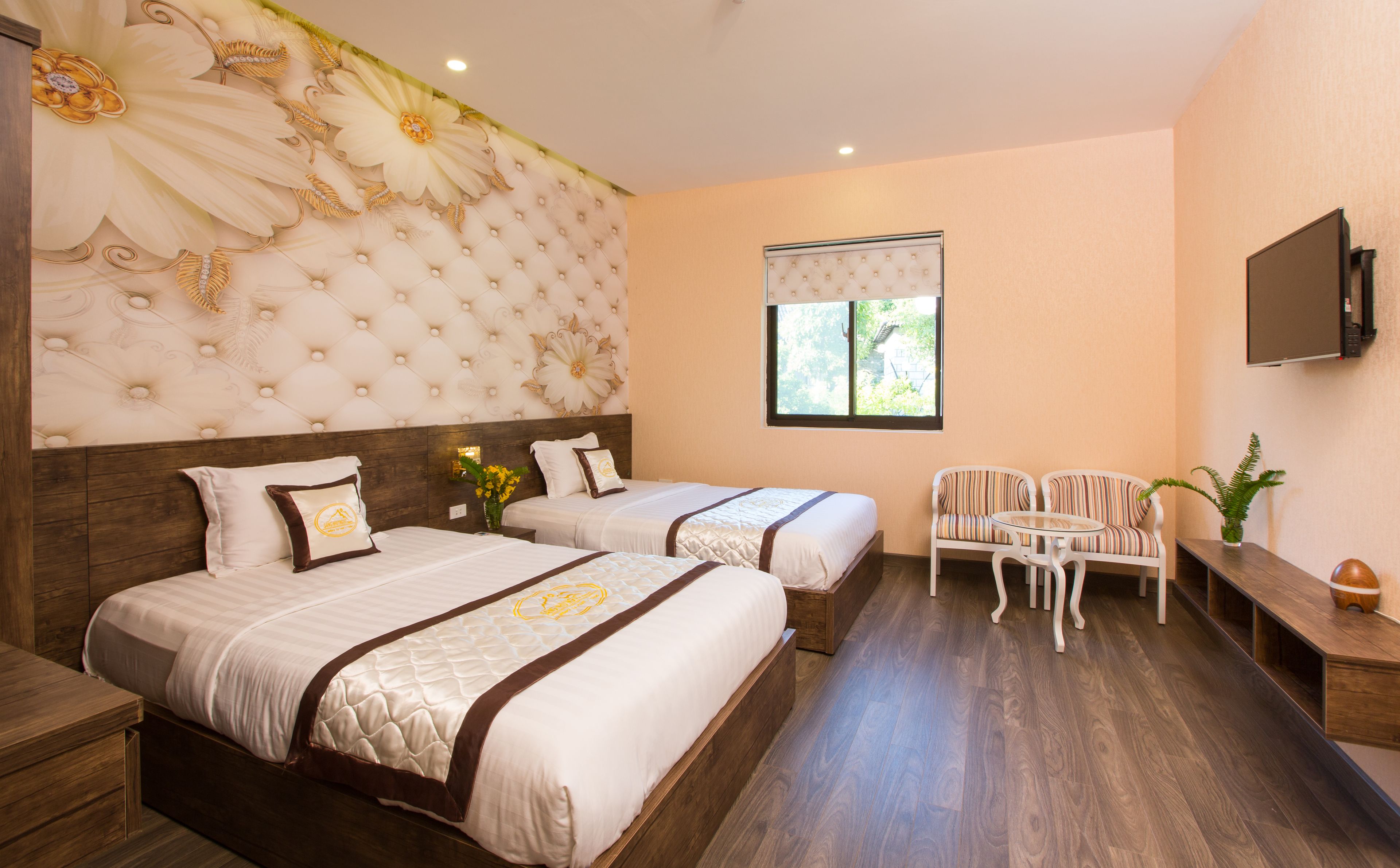 A hotel room with two beds, a TV, a window, and a seating area.