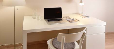 A white desk with a laptop, a lamp, and a chair with a cushion.