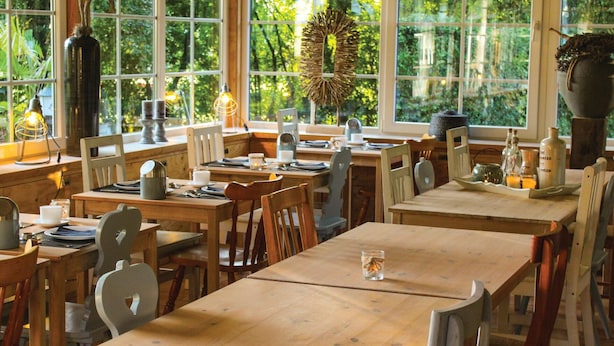 A restaurant with wooden tables and chairs, large windows with a view of greenery, and various table settings. - Awesome apartment in Simpelveld with outdoor swimming pool (Simpelveld)