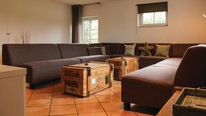 A living room with a sectional sofa, wooden crates, and a window with blinds. - Awesome apartment in Simpelveld with outdoor swimming pool (Simpelveld)