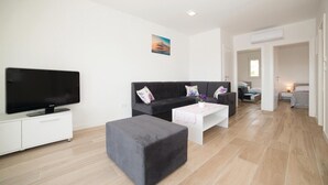A modern living room with a flat-screen TV, a dark sofa, a white coffee table, and a grey ottoman. - Nice apartment in Trogir with WiFi (Trogir)