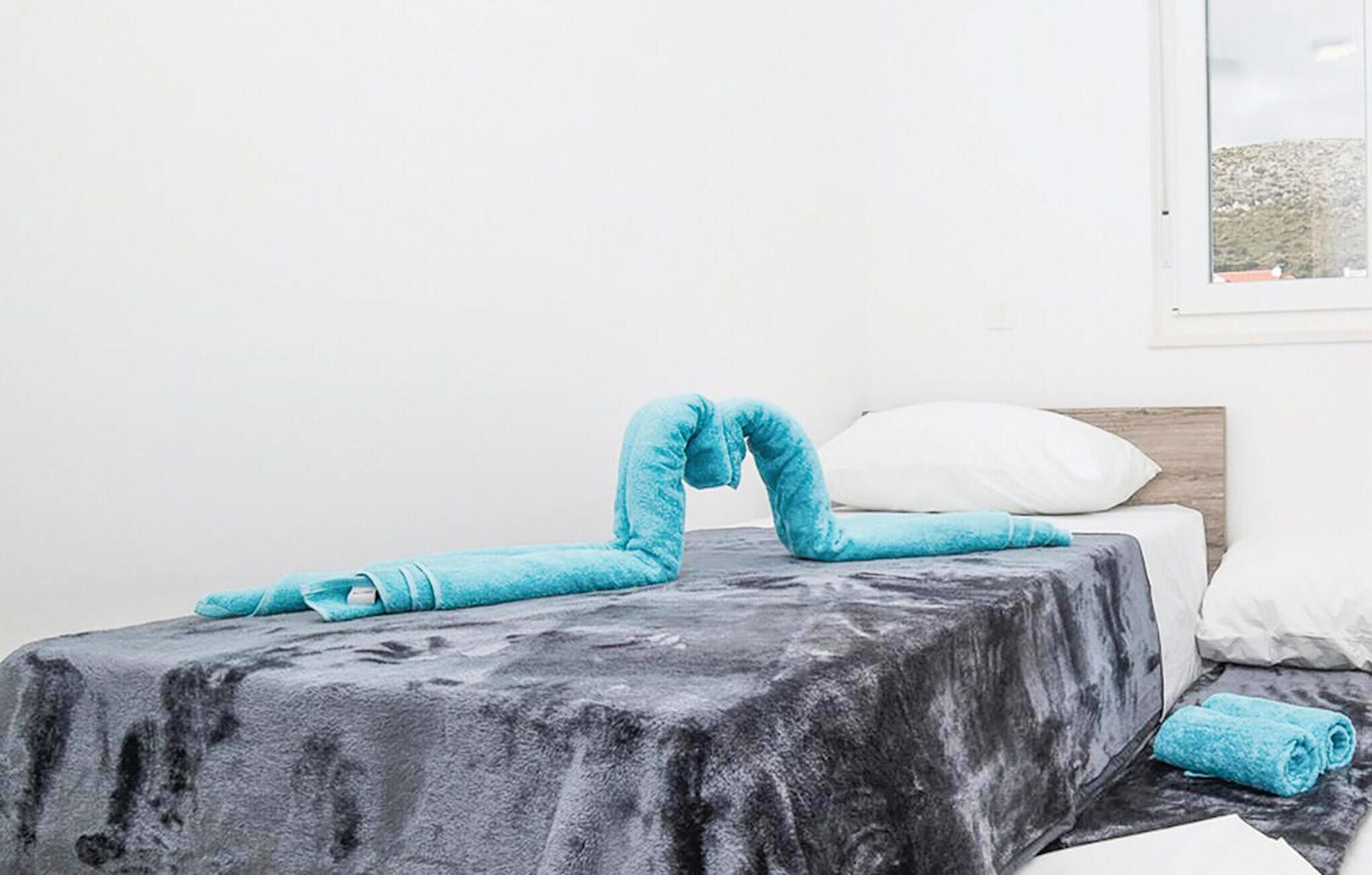 A bed with a grey blanket, a white pillow, and a blue towel.