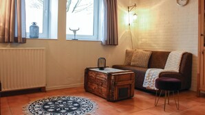 Una sala de estar acogedora con un sofá marrón, un pequeño cofre de madera, un tapete estampado y un reloj de pared.