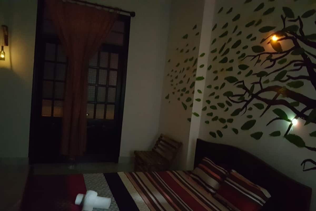 Ein Zimmer mit einem Bett, einem Sessel, einem Fenster mit Vorhängen und einer Wand mit Wandgemälde eines Baumes.