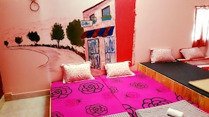 Quarto com cama, almofadas, janela e um mural na parede.