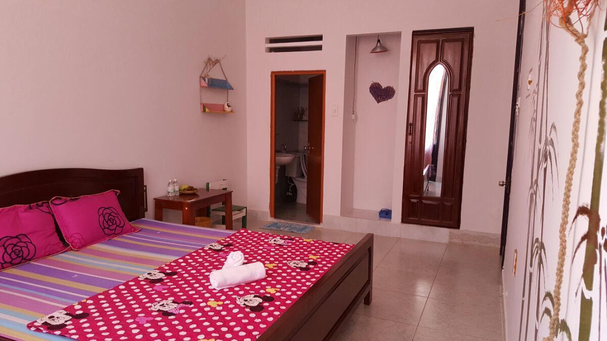 A bedroom with a bed, a bedside table, a nightstand, a dresser, a mirror, and a door leading to a bathroom.