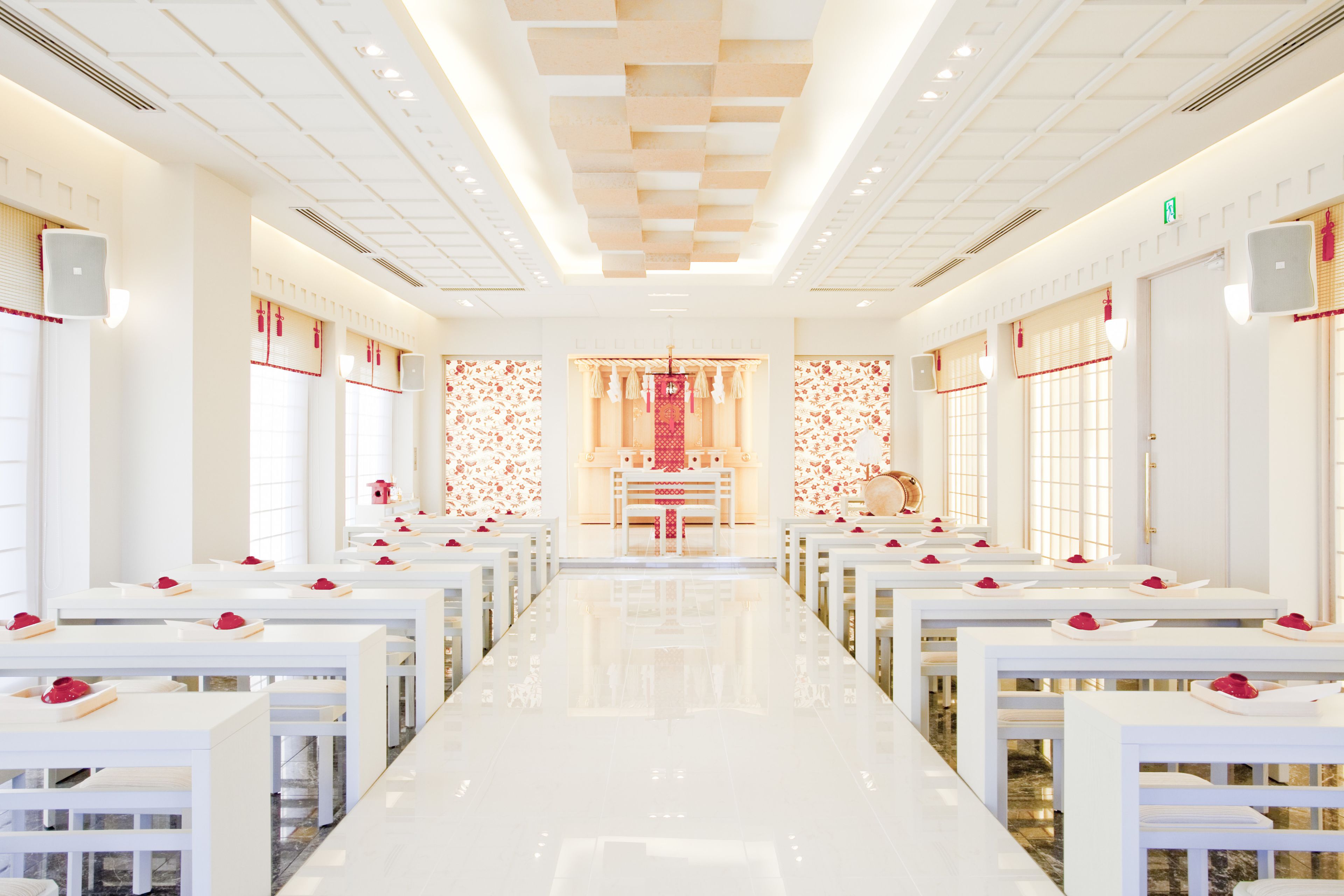 A hotel lobby with a long, reflective floor, rows of white tables, and a central reception area with a red and gold decor.