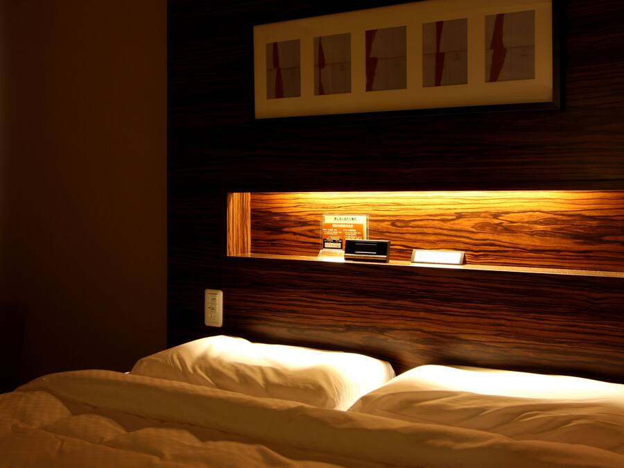A hotel room with a wooden headboard, a bedside table with a lamp, and a framed picture above the bed.