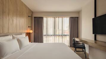 A hotel room with a large bed, a desk, a chair, a TV, and a window with curtains.