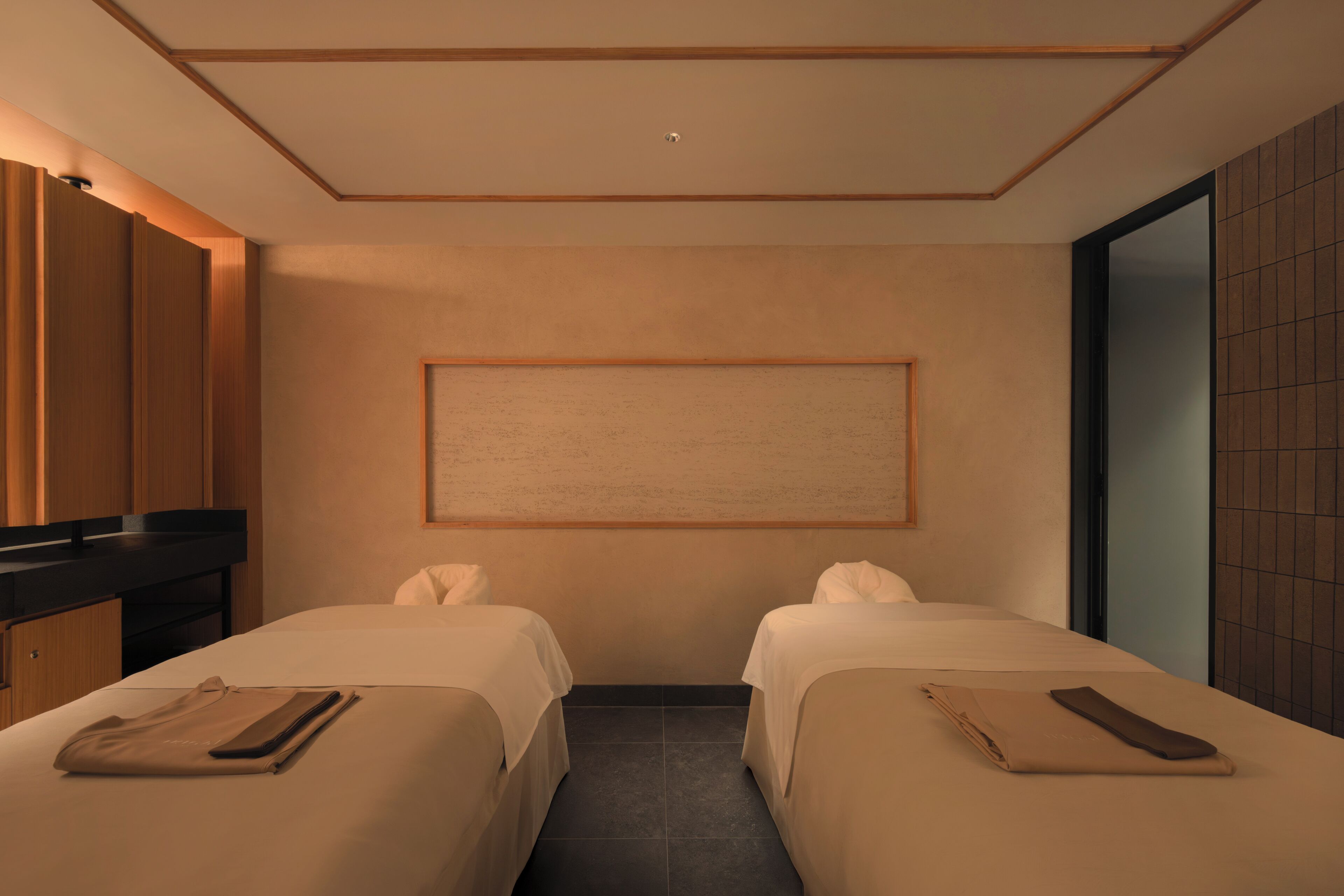 A hotel room with two beds, a large mirror, and a framed artwork on the wall.