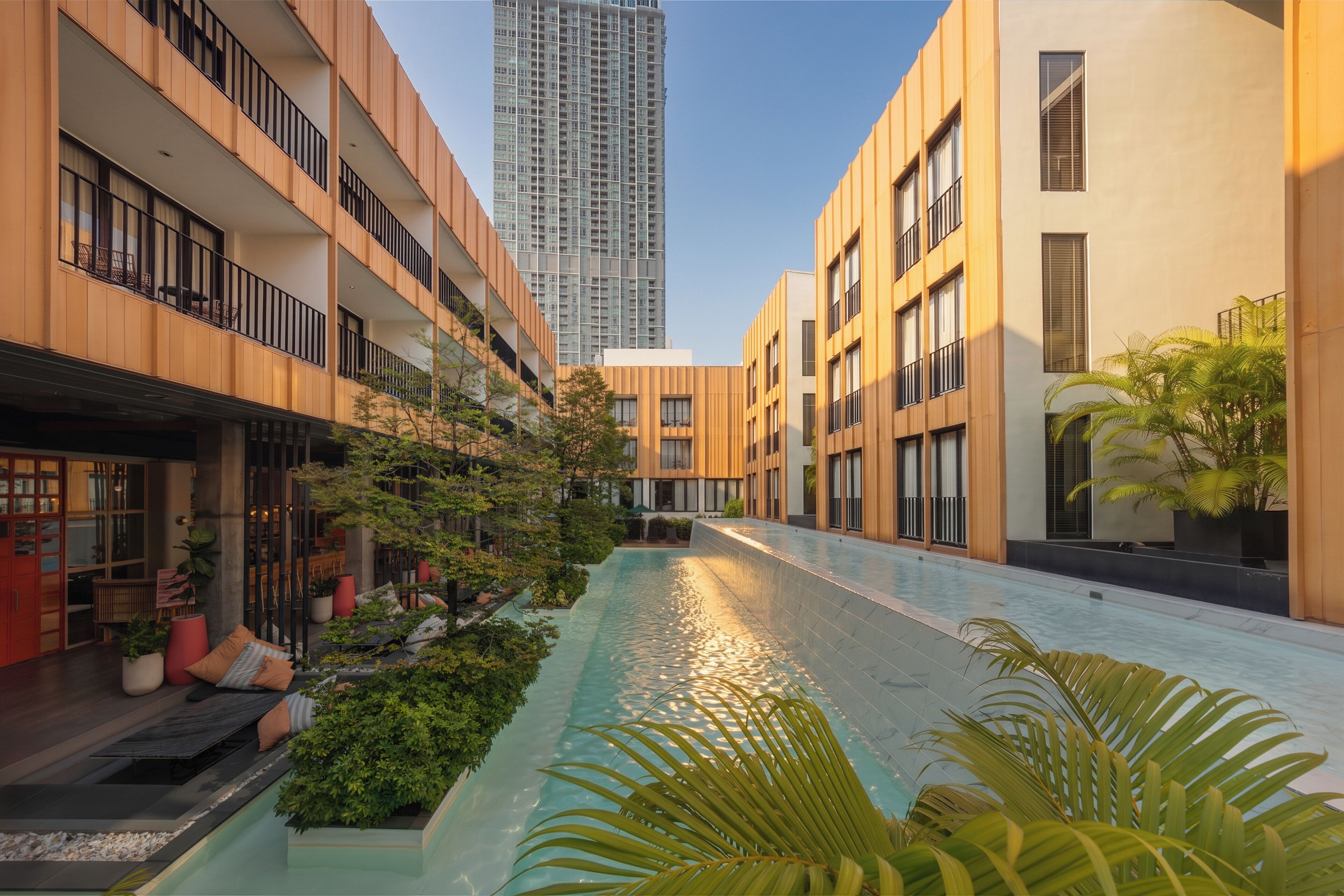 A modern building with a swimming pool, outdoor seating, and a tall skyscraper in the background.