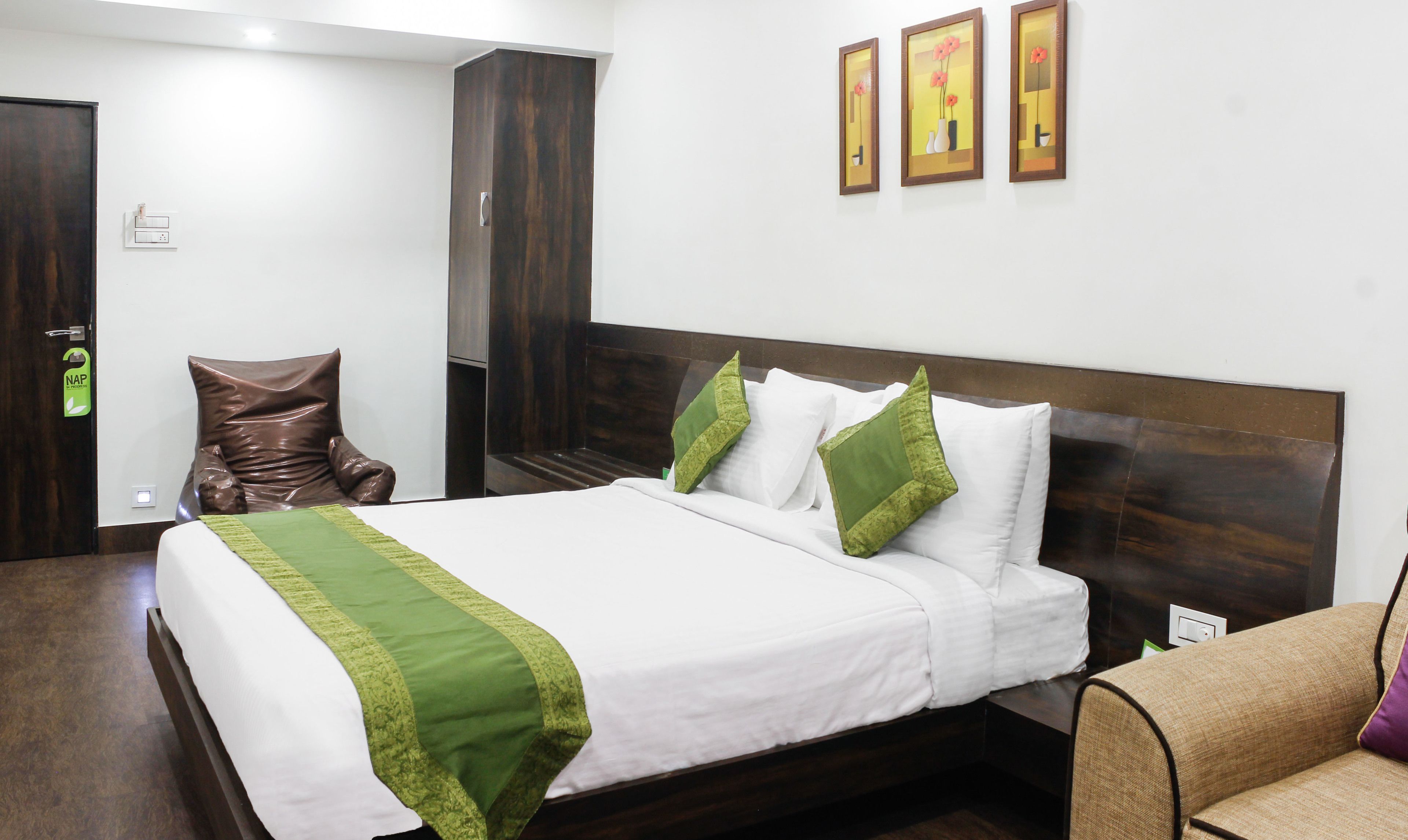 A neatly made bed with white and green linens, a wooden headboard, and a brown armchair.