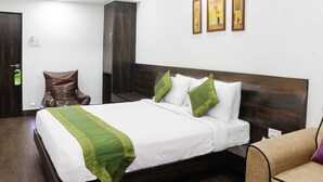 A neatly made bed with white and green linens, a wooden headboard, and a brown armchair. - Hotel Indralok Inn (Mawal)