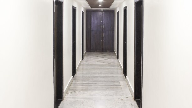 A hallway with white walls, black-framed doors, and a marble floor. - Hotel Indralok Inn (Mawal)