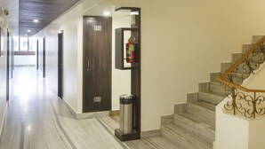 A hallway with a marble floor, a fire extinguisher mounted on a wall, and a staircase with a metal railing. - Hotel Indralok Inn (Mawal)