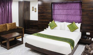 A hotel room with a bed, a sofa, a small table, and a nightstand with a phone. - Hotel Indralok Inn (Mawal)