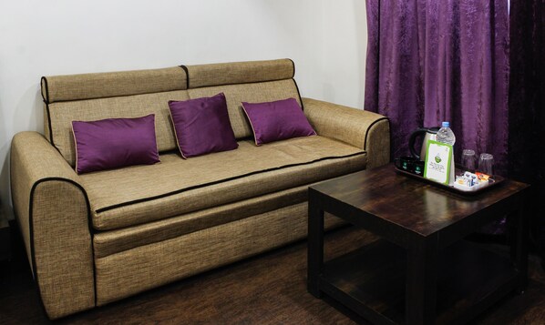 A sofa with a cushion, a coffee table, and a tray with a kettle, cups, and a bottle.