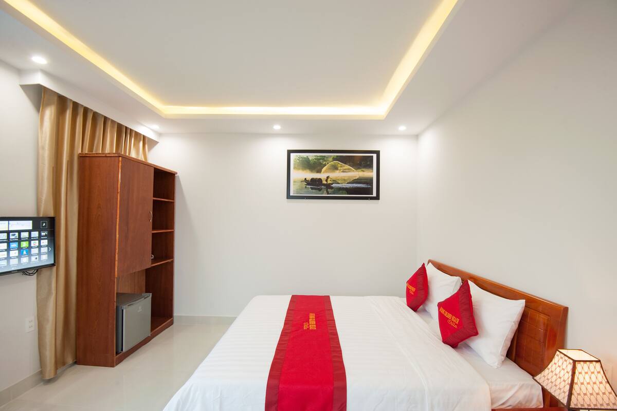 A hotel room with a bed, a wooden wardrobe, a flat-screen TV, and a framed picture on the wall.