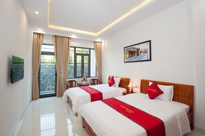 A hotel room with two beds, a TV, a window with curtains, a framed picture on the wall, and a table with a vase of flowers. - An Bang Golden Beach Villa (Da Nang)
