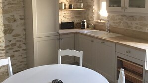 A small kitchen with a round table, white chairs, a white refrigerator, and a stone wall. - In the heart of downtown St Rémy de Provence, the Mas D'Oscar! (Saint-Rémy-de-Provence)