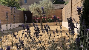 A garden with lavender and other plants, a wooden fence, and a building with a tiled roof. - In the heart of downtown St Rémy de Provence, the Mas D'Oscar! (Saint-Rémy-de-Provence)