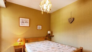 A bedroom with a wooden bed, a nightstand with a lamp, and two framed pictures on the wall. - La Clusaz - 6 pers - 2 Bdr - Near slopes - Garage (La Clusaz)
