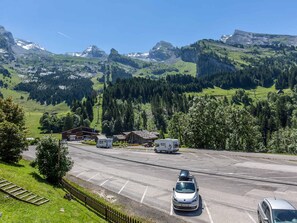 A parking lot with vehicles, a building with a sloped roof, and a mountainous landscape in the background. - La Clusaz - 6 pers - 2 Bdr - Near slopes - Garage (La Clusaz)