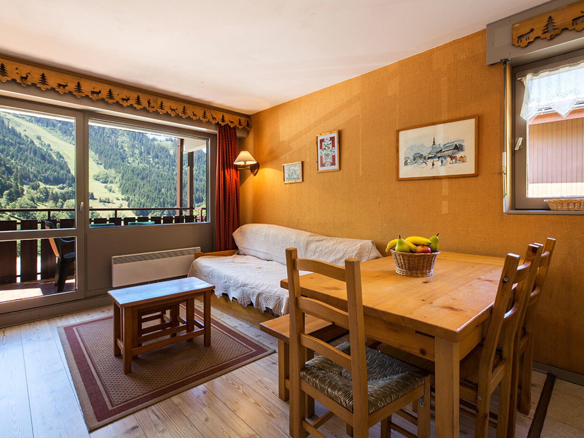 Ein Essbereich mit Holztisch, Stühlen, einer Bank und Blick auf eine Berglandschaft durch große Fenster.