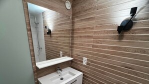A modern bathroom with a wooden wall backsplash, a white vanity with a mirror, and a built-in shower. - La Clusaz - 6 pers - 2 Bdr - Near slopes - Garage (La Clusaz)