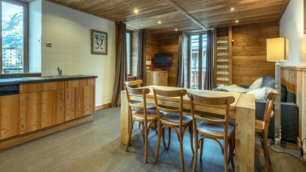 Ein gemütliches Blockhaus-Interieur mit einem Essbereich aus Holz, einer Küche mit Holzschränken und einem Wohnbereich mit Sofa und Fernseher.