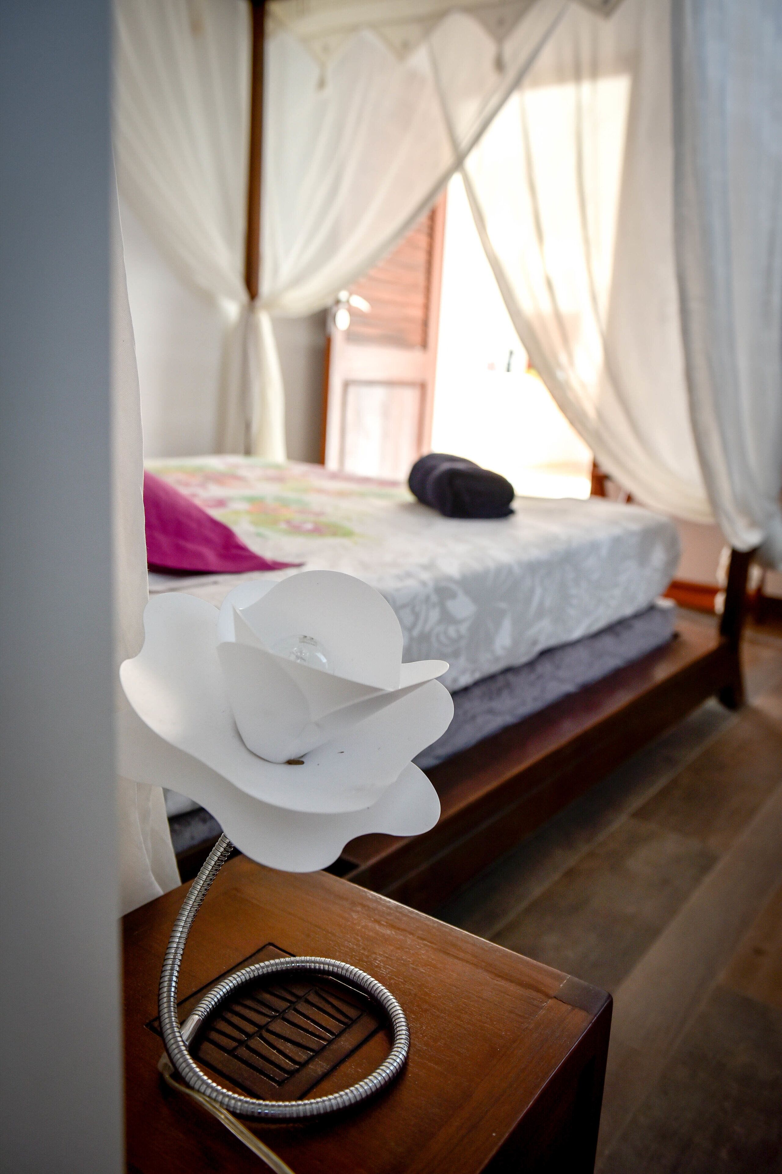 A bed with a white canopy, a wooden nightstand with a telephone, and a pink pillow on the bed.