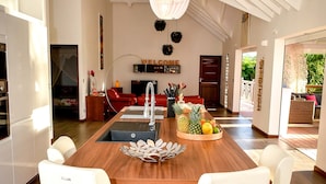 A spacious kitchen with a central island, white bar stools, and a fruit bowl. - 5* Villa with Secured Pool and Beautiful Tropical Garden (SAINT FRANCOIS)