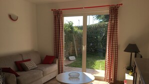 Una sala de estar con un sofá, una mesita redonda y vistas a un jardín a través de una puerta corrediza de vidrio.