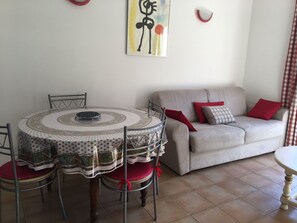 Un coin repas avec une table ronde et des chaises, un canapé avec des coussins et un mur orné d’un tableau.
