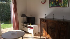 Una habitación con una mesa de comedor, un televisor sobre un mueble blanco, un armario de madera con tiradores decorativos y un cuadro en la pared.