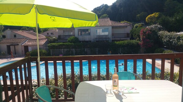 Une vue sur la piscine, avec une terrasse en bois, une table avec des verres et une bouteille, et un parasol jaune.
