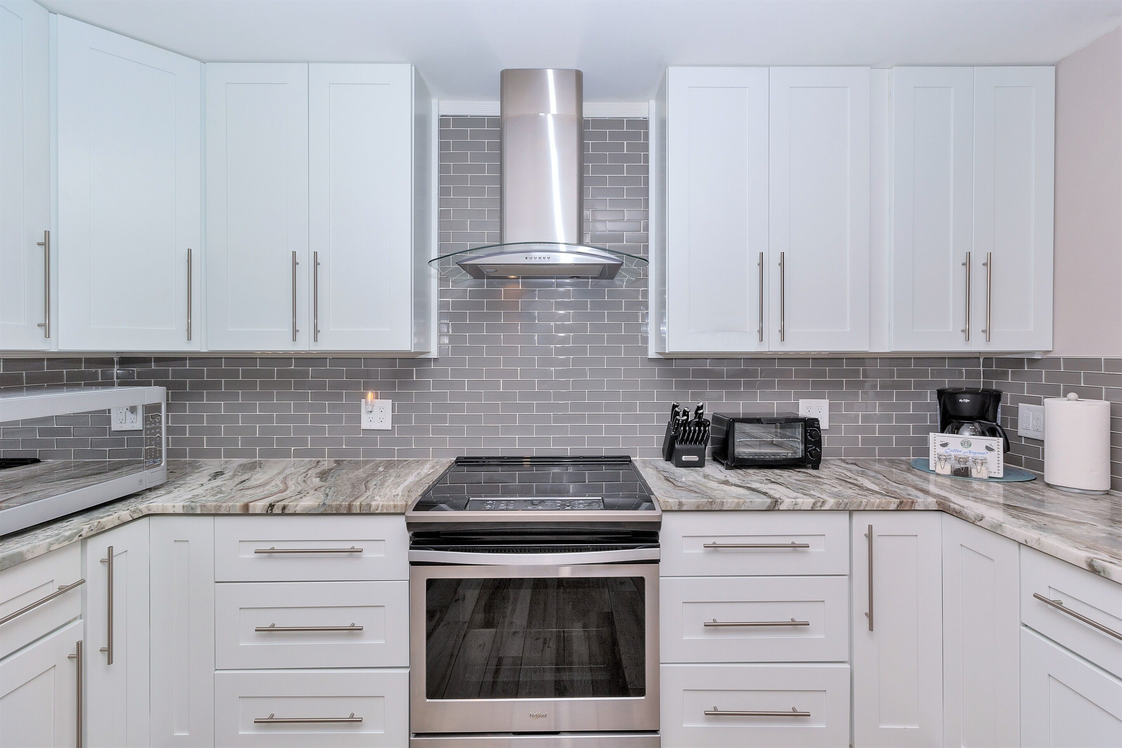 A modern kitchen with white cabinets, a stainless steel range, and a brick backsplash.