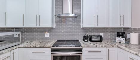 A modern kitchen with white cabinets, a stainless steel range, and a brick backsplash.