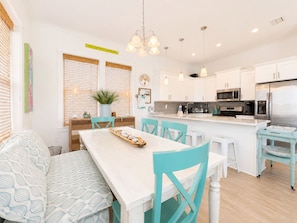 A modern kitchen with white cabinets, stainless steel appliances, a central island, and teal chairs.