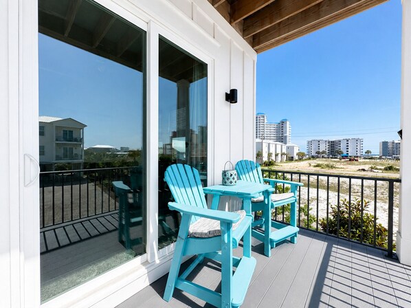 A balcony with two chairs and a table, overlooking a beach and buildings.