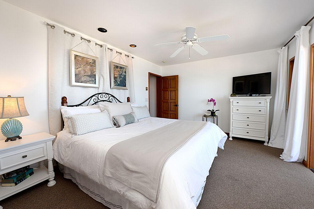 A bedroom with a bed, a nightstand, a dresser, a television, and a ceiling fan.