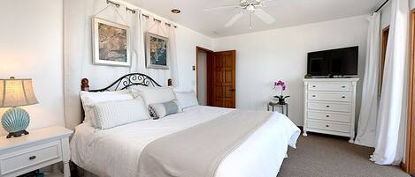 A bedroom with a bed, a nightstand, a dresser, a television, and a ceiling fan.