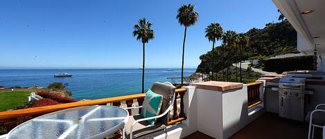 Ein Balkon mit Tisch und Stühlen, einem Grill und Blick auf das Meer und Palmen.