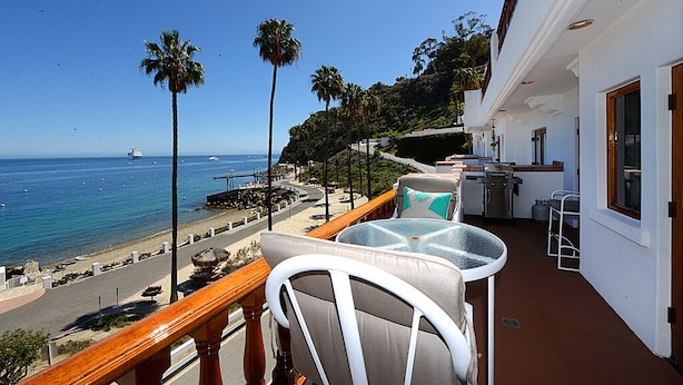 A balcony with a view of the ocean, palm trees, and a building with a white exterior. - H881: Beautiful Townhouse style villa + CART+ 2 Private Balconies + King bed (Avalon)