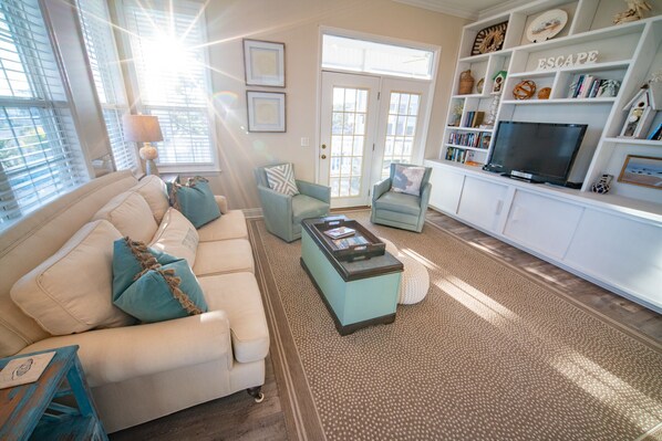 A living room with a beige sofa, teal armchairs, a coffee table, and a bookshelf with decorative items. - Beach Retreat, Easy Beach Access, Gulf Views & Private Pool! (St. George Island)