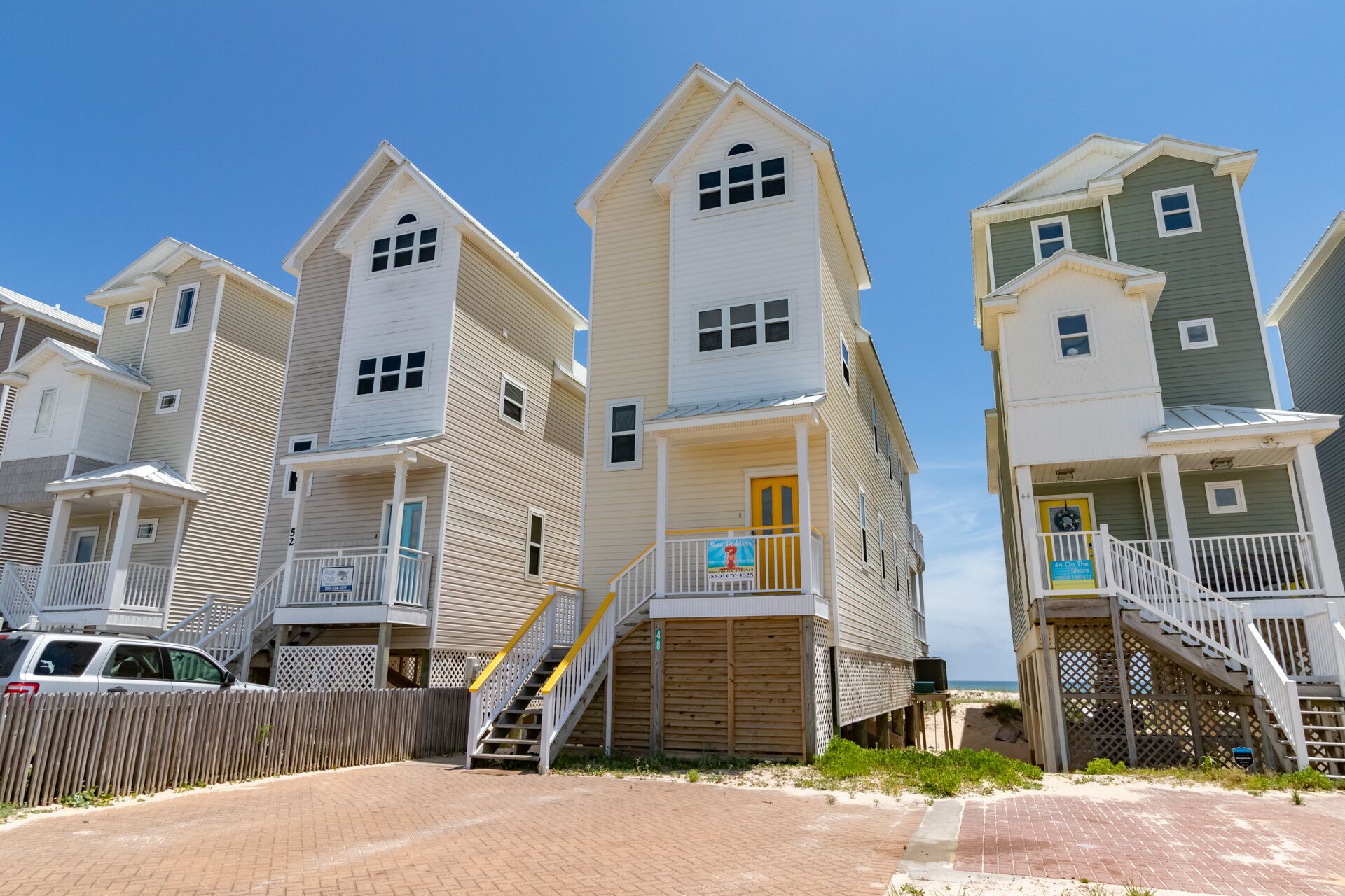 A row of beach houses with balconies, wooden decks, and a sandy beach in the background.